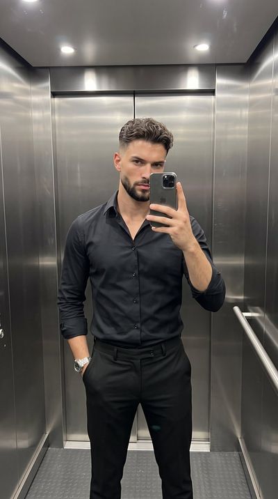 Man in black shirt takes mirror selfie inside sleek elevator
