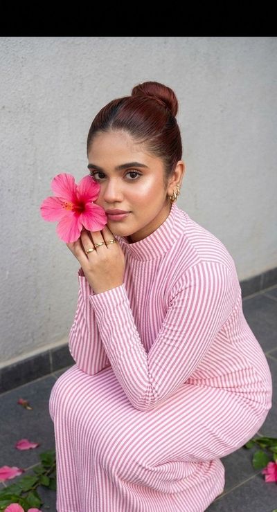 A girl in a pink striped dress presses a hibiscus to her cheek.