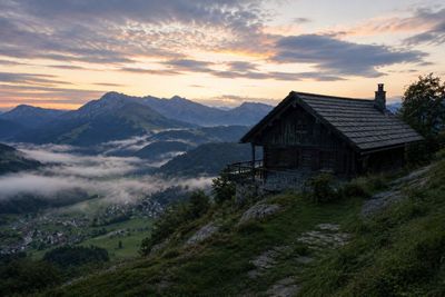 Golden sunrise illuminates jagged peaks above misty alpine cabin