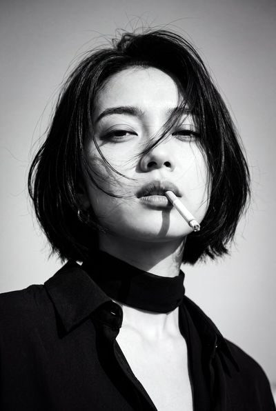 A windswept woman holds a cigarette in a 1970s noir portrait