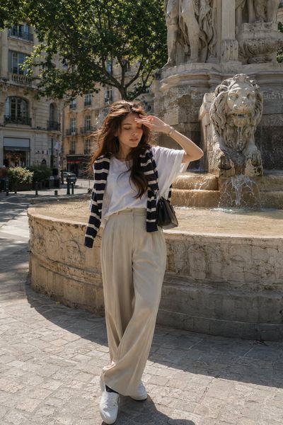 Young woman poses by Parisian fountain in effortless French chic style