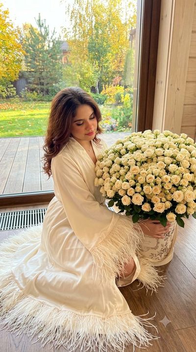 Woman in Silk Robe Sits on Wooden Floor with Cream Roses
