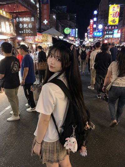 A young girl in a cat headband explores a neon-lit night market.