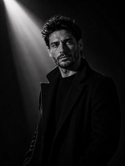 A solitary man in a black coat stands in diagonal light.