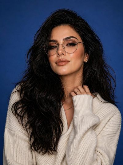 Woman in oversized sweater poses confidently against blue studio backdrop