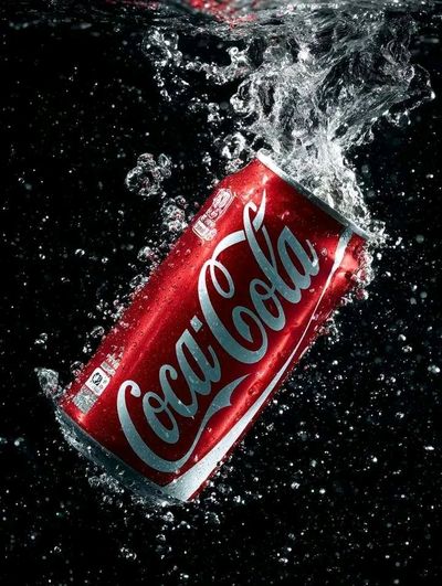 A glossy soda can erupts with water splashes against black background
