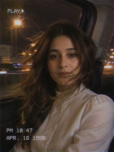 Young woman rides in backseat with city lights streaming behind her.