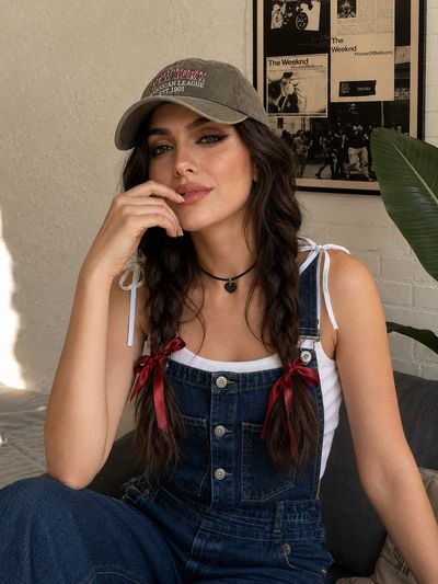 Young woman in denim overalls smiles softly indoors