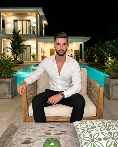 Confident man in white shirt relaxes on lounge chair at night poolside