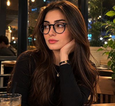 A thoughtful woman with dark hair rests in a cozy café at night.