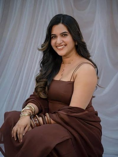 Indian woman with warm smile poses in satin dress with gold jewelry