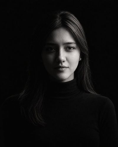 Woman in black turtleneck poses against dark studio background