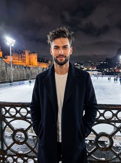 Young man in navy coat smiles by snowy railing at night rink