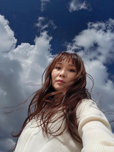 A woman stands centered under a vast blue sky with clouds