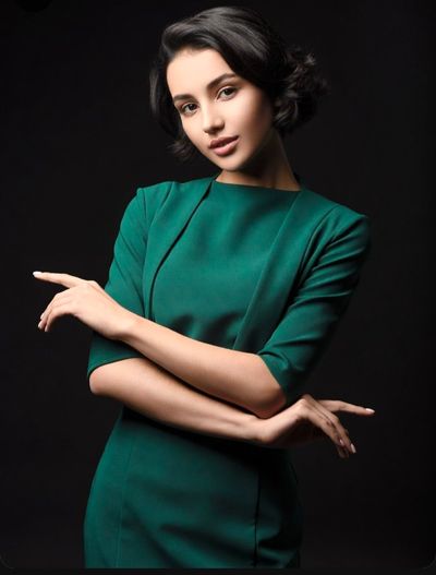 Elegant woman in green dress crosses arms in studio portrait