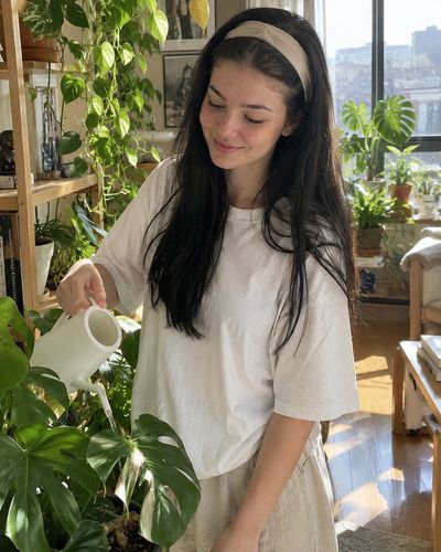 Young woman waters lush houseplants in sunlit cozy apartment