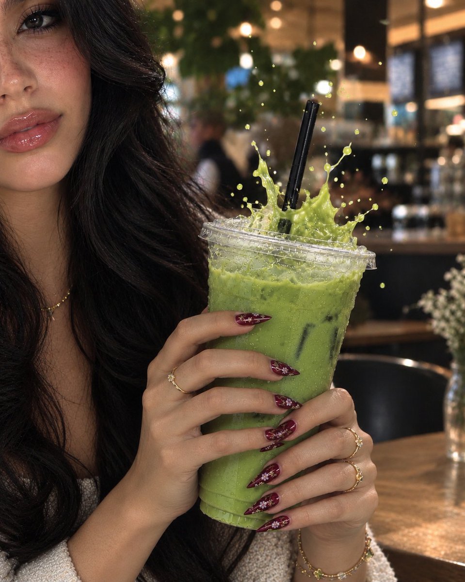Woman with burgundy nails holds iced matcha latte in cozy café