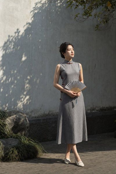 Young woman in slate qipao stands by shadowed wall