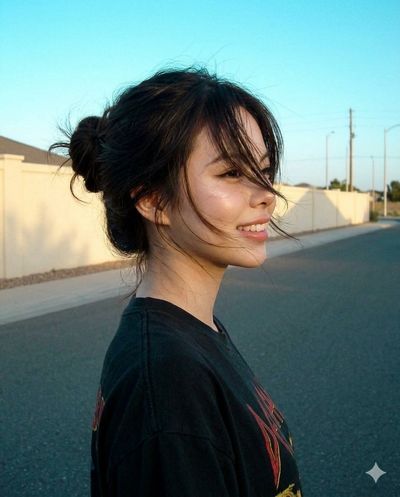 A woman in a black band tee stands on a quiet street during golden hour