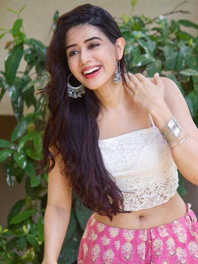 Indian woman with wavy hair smiles in garden wearing white lace