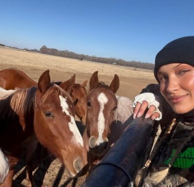 A woman in a beanie leans on a fence with three horses