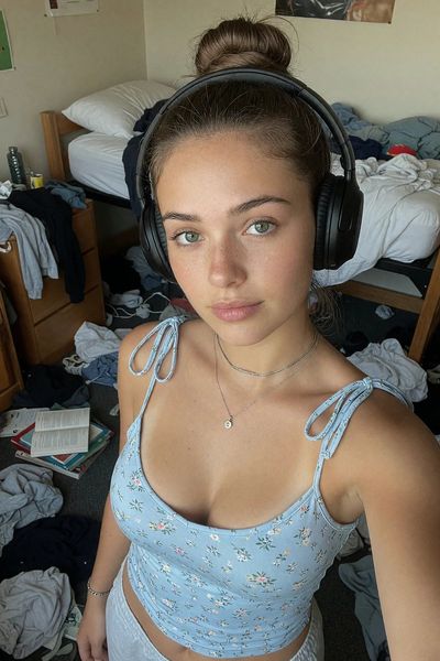 Young woman in blue camisole takes a high-angle selfie in messy dorm room