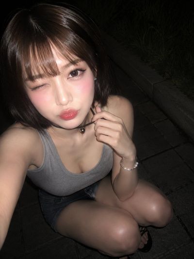 Young woman winks in a nighttime flash selfie crouching on sidewalk