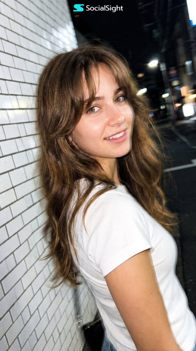 Young woman walks past flashing smartphone camera on dark Tokyo street