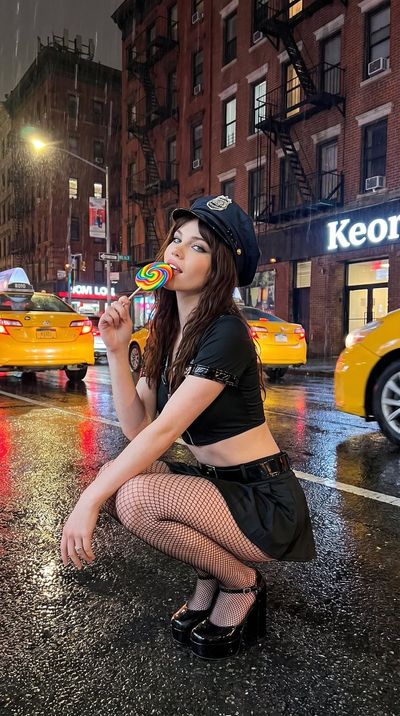 A playful policewoman in fishnets crouches on a rainy New York street.