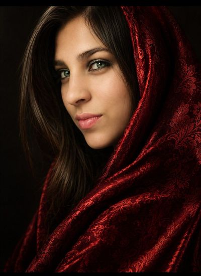 Woman in red velvet hood gazes with serene green eyes