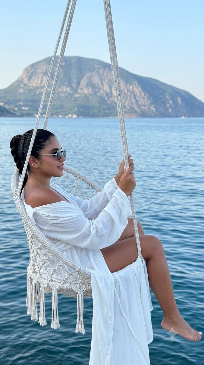 A woman relaxes in a macrame chair above the calm sea.