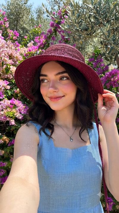 A young woman in a maroon hat smiles among purple flowers
