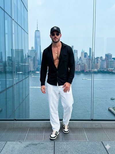 Confident man in black shirt poses on outdoor deck overlooking Manhattan skyline