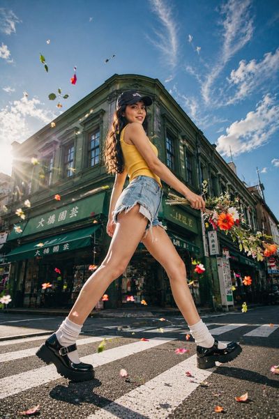 Model with yellow tank top drops flowers on sunlit crosswalk