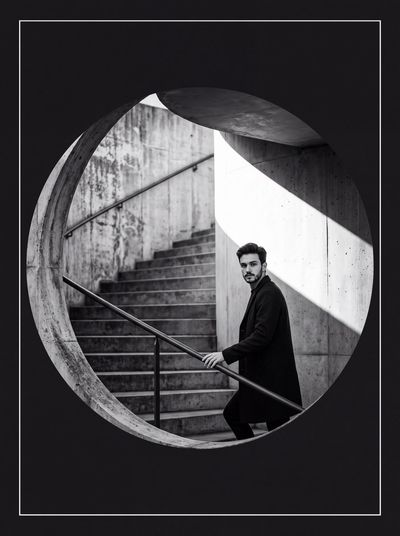 Man Ascending Brutalist Stairwell Looks Back Through Circular Porthole