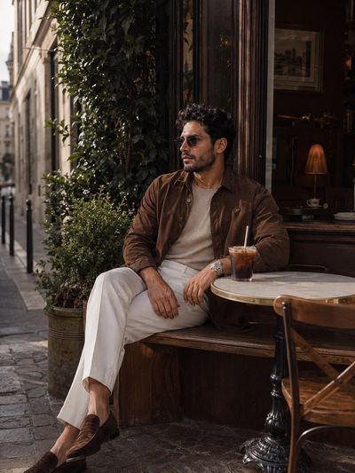 A stylish man in brown suede sits at a European café