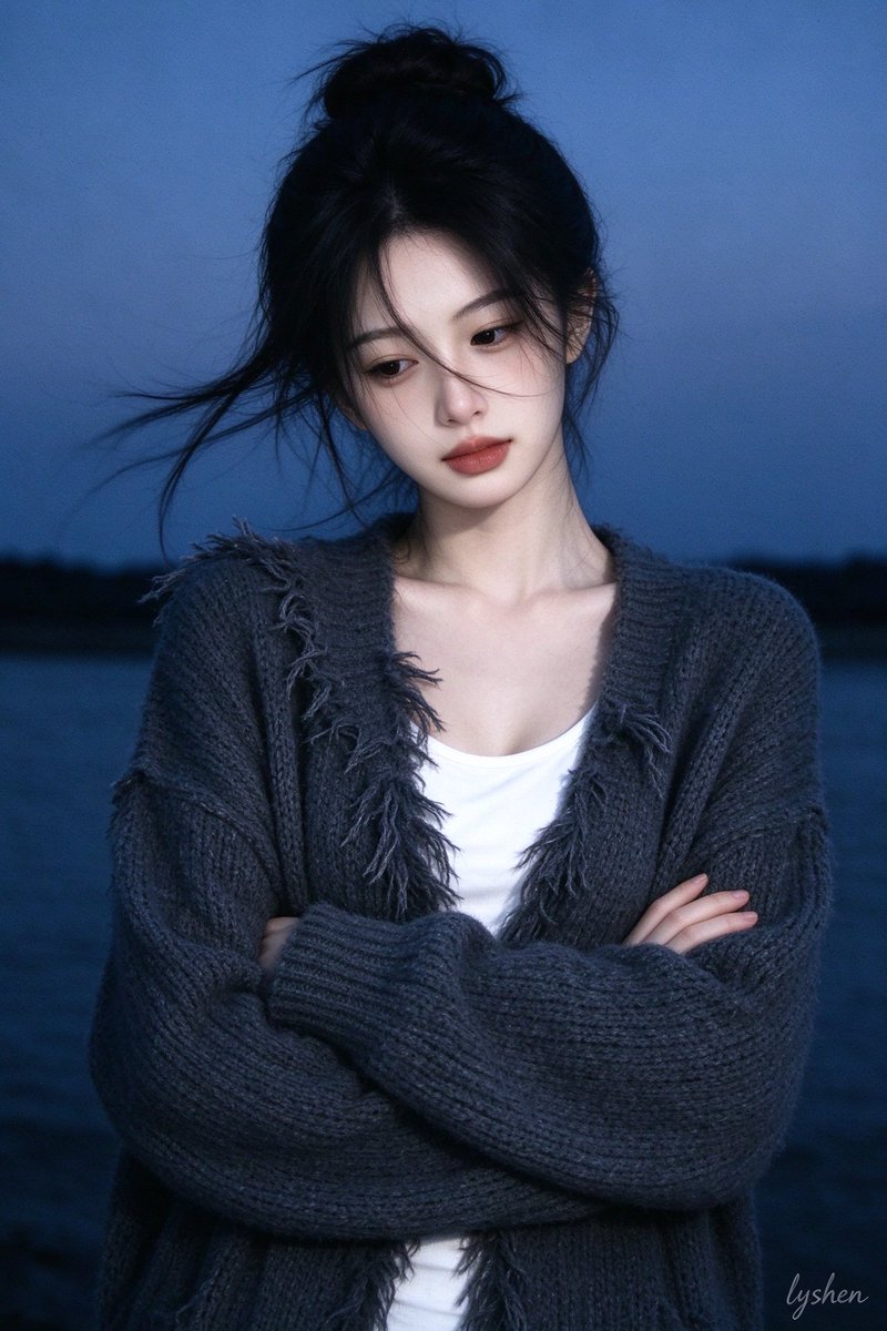 Young woman in charcoal cardigan stands against blue dusk