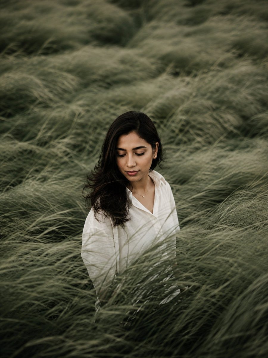 A solitary figure stands lost in wind-swept sage green fields.