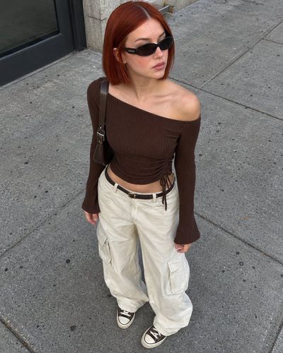 Auburn-haired woman in brown top stands on sunlit city sidewalk