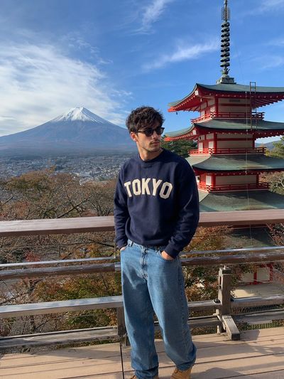 A man in navy sweater views Mount Fuji from a wooden deck