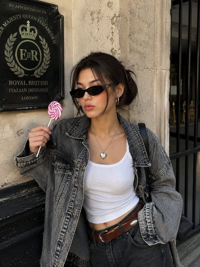 Korean woman in denim jacket poses with lollipop against vintage wall
