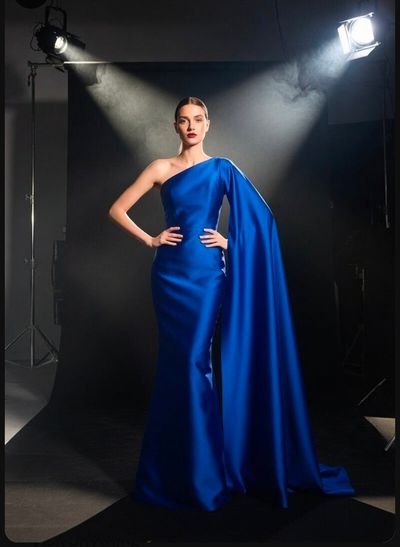 A model in a royal blue gown poses under dramatic studio light