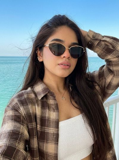 Confident girl in sunglasses poses against turquoise sea with windblown hair