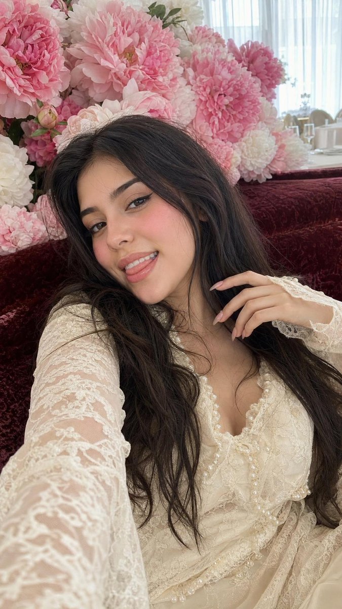 Woman reclines on velvet sofa amidst blush peonies in candid selfie