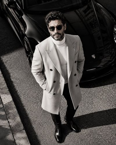 A confident man in an overcoat stands by a luxury car