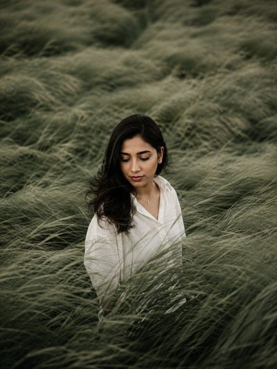 A solitary figure stands lost in wind-swept sage green fields.