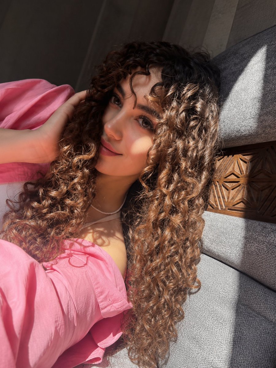Woman with dark curls sits on cream sofa in golden sunlight