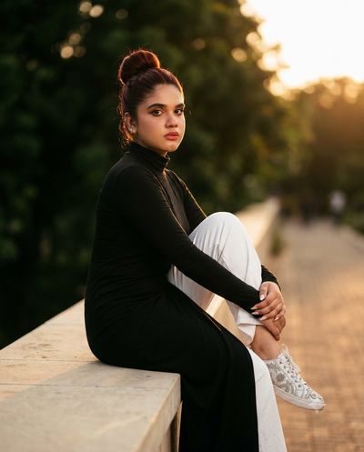 A young woman sits sideways on a stone ledge in warm sunset light.
