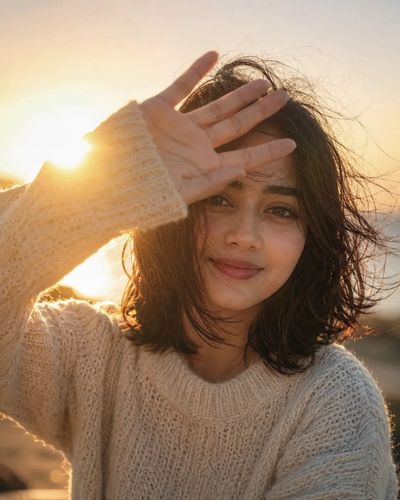 A young woman smiles softly in warm sunset light with lens flare.
