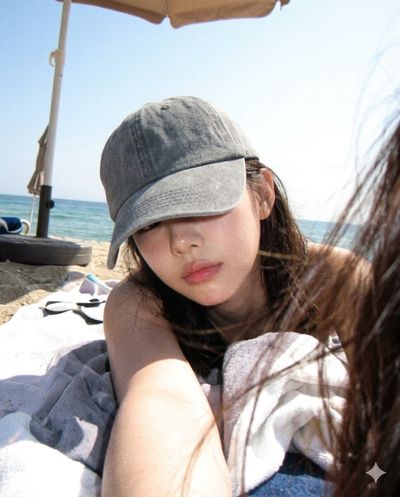A woman in a baseball cap traces patterns on a towel by the sea
